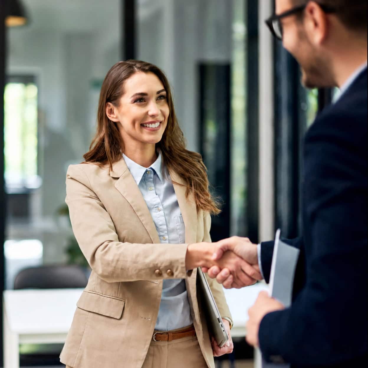 a business woman advisor shaking hands with a professional man while they are both holding paperwork and their computers